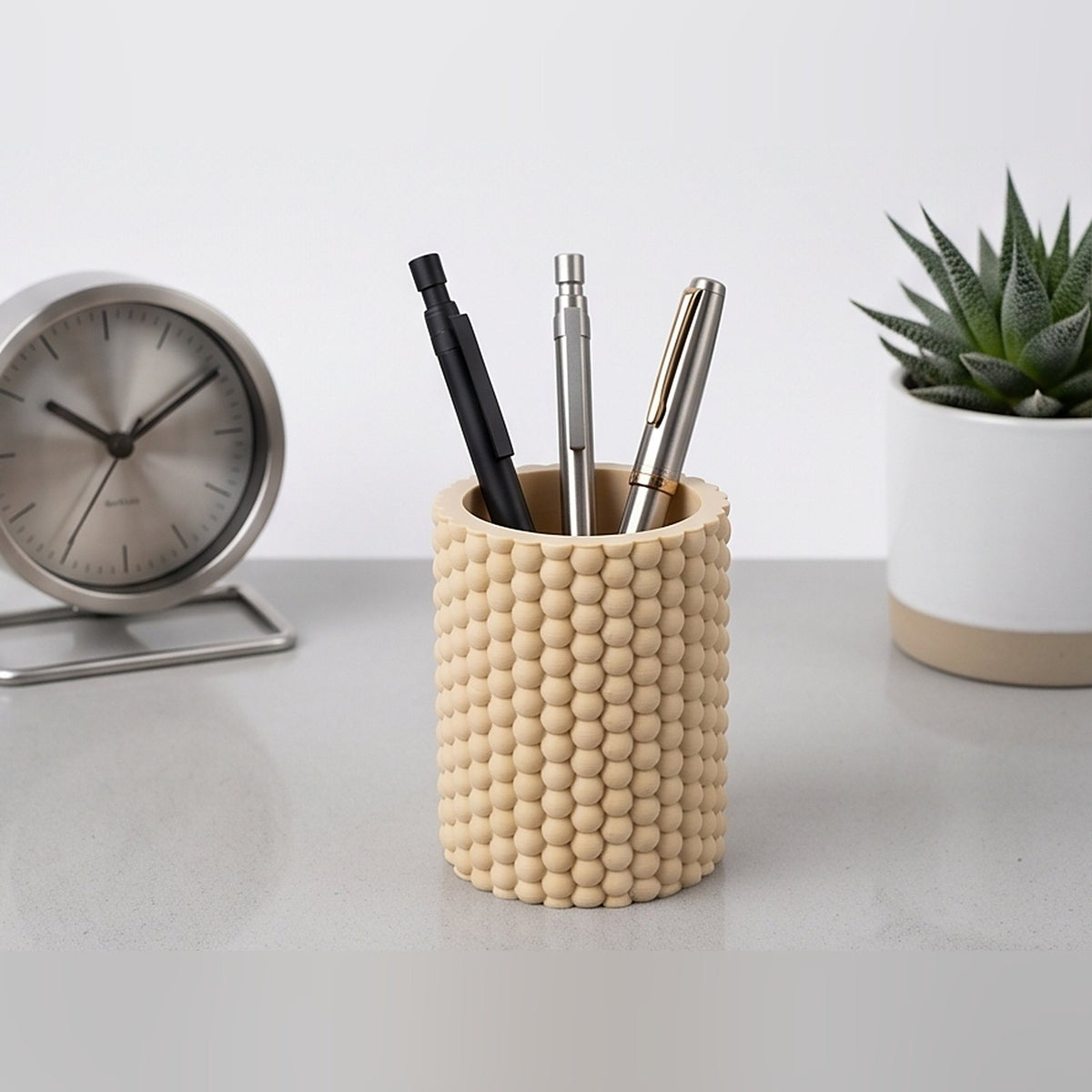 Bobble pen pot on a light desk holding three pens, beside a clock and a succulent