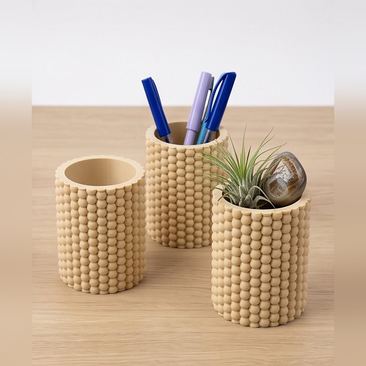 Three bobble pen pots on a wooden table holding pens and an air plant