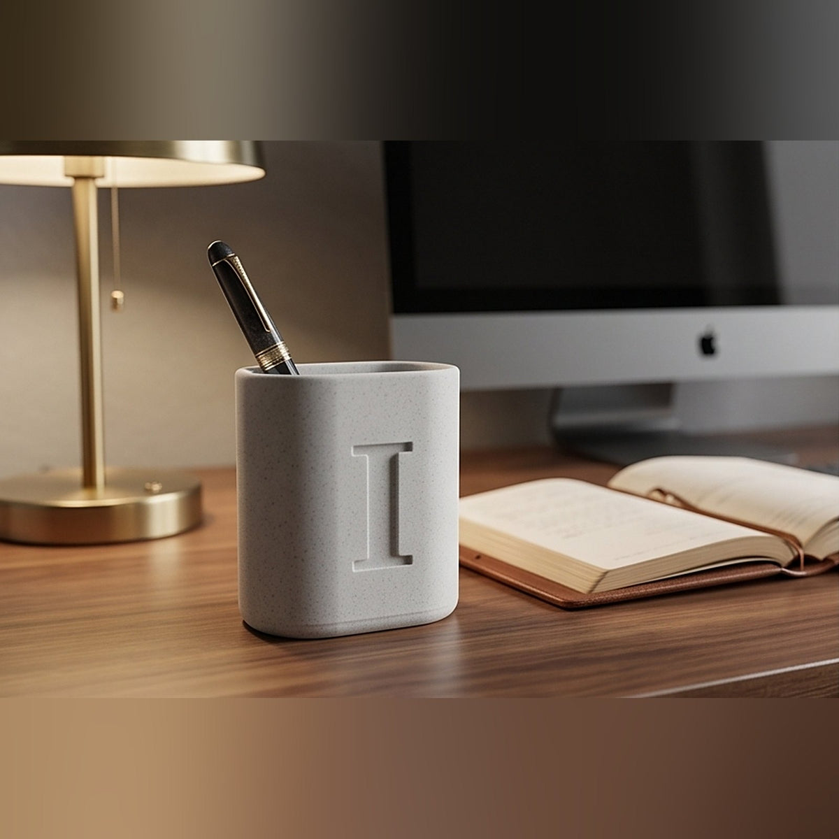 Marble monogram pen stand on a walnut desk beside a brass lamp, holding a fountain pen