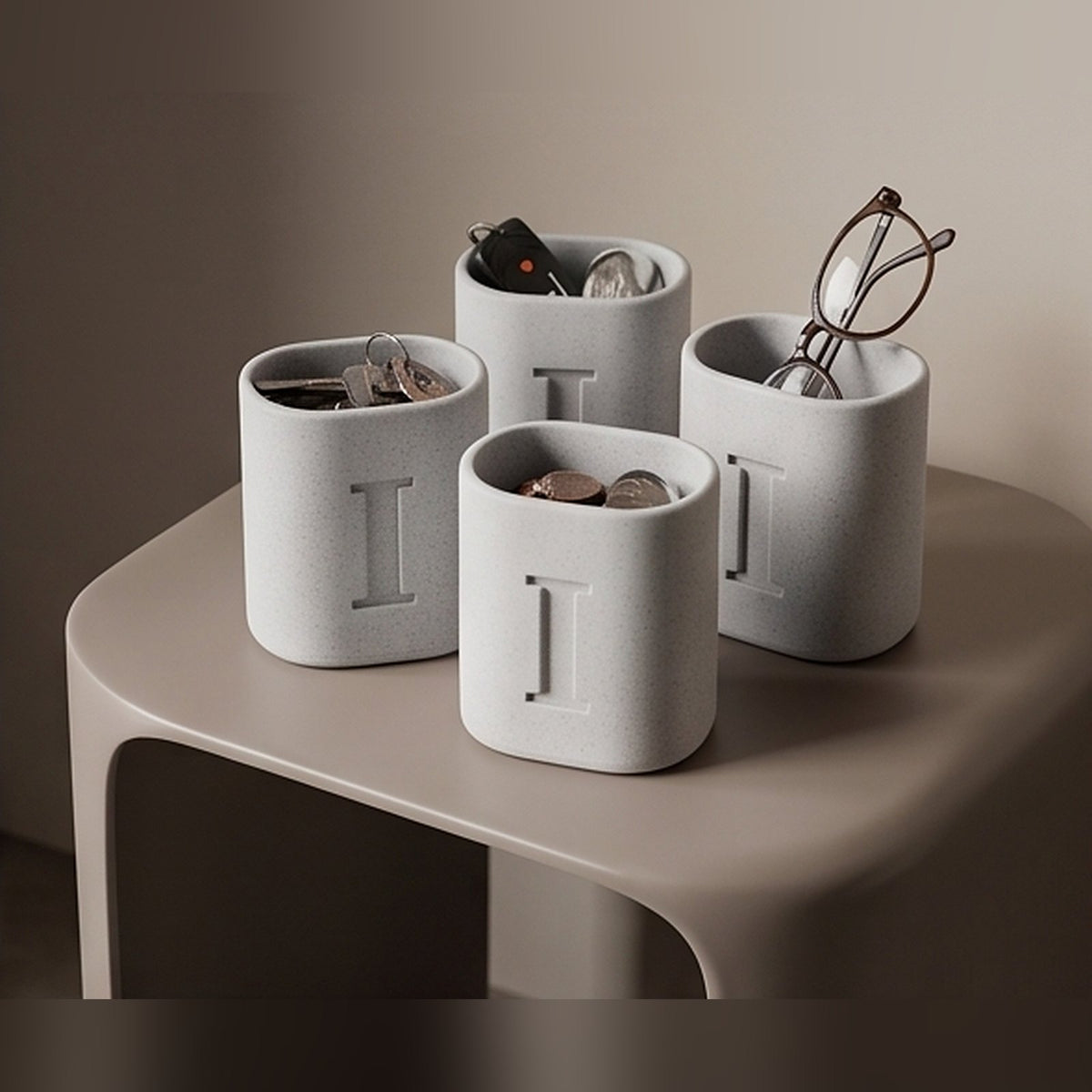 Four marble monogram pen stands on a side table holding keys, coins and glasses