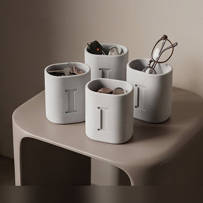 Four marble monogram pen stands on a side table holding keys, coins and glasses